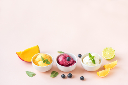 Three various fruit and berries ice creams on pink background, copy space. Frozen yogurt or ice cream with lemon, mango, blueberries - healthy summer dessert.の写真素材