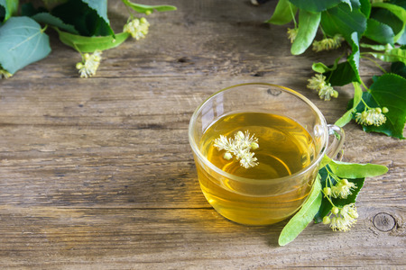 Healthy herbal linden tea with bunch of fresh linden flowers on wooden background. Cup of organic linden tea, herbal drink.の写真素材