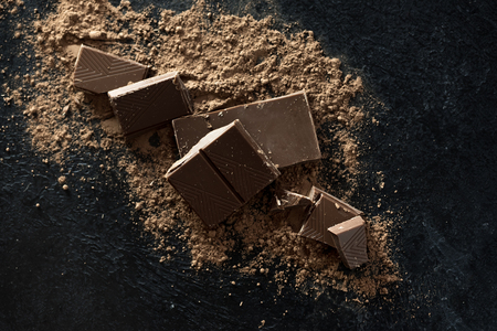 Broken chocolate pieces and cocoa powder on black. Chunks of chocolate onr dark stone background.の写真素材