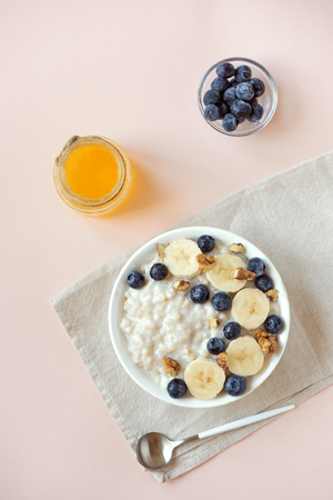 Oatmeal porridge with walnuts, blueberries and banana in bowl on pink pastel background - healthy organic breakfast, oats with fruits, honey and nutsの写真素材