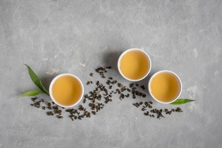 Green tea in ceramic cups, dry green oolong tea and tea leaves on grey stone table, top view, copy...