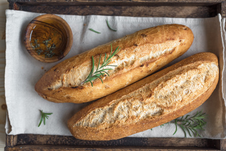 Fresh homemade bread with rosemary and extra virgin olive oil in rustic wooden box, top view. Sourdough mini baguette bread.の写真素材