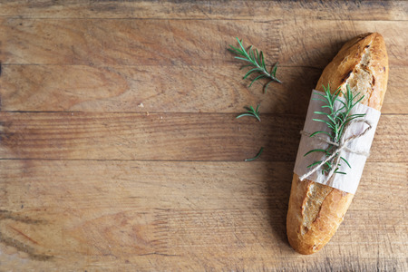 Fresh homemade bread with rosemary on rustic wooden background, top view, copy space. Sourdough mini baguette bread.の写真素材