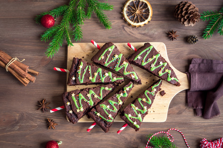 Chocolate Brownies in shape of Christmas Trees with green icing and festive sprinkles on wooden table, top view. Sweet homemade Christmas or winter holidays pastry food concept.の写真素材