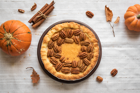 Pumpkin and Pecan Pie with cinnamon on white linen background, top view, copy space. Homemade autumn pastry for Thanksgiving.の写真素材