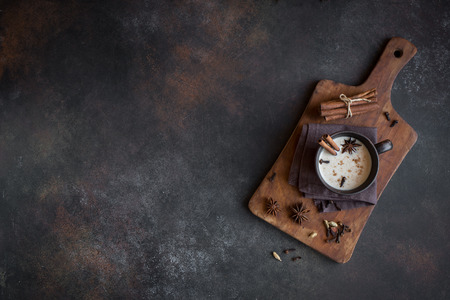 Traditional indian masala chai tea in ceramic cup with ingredients. Spicy black tea with milk on rustic dark background, copy space.の写真素材