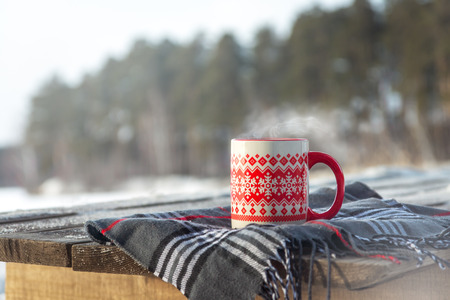 Steaming Cup of Hot Coffee or Tea standing on the Outdoor Wooden Table in Snowy Winter Day. Winter weekend or holidays, Christmas morning, healthy activities outdoor concept.の写真素材