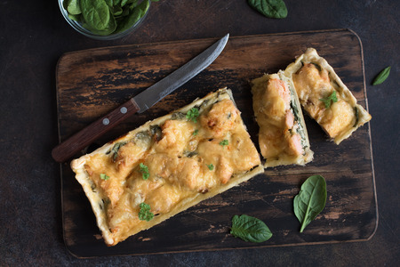 Salmon Spinach Pie (quiche) with cheese on dark rustic background. Homemade salmon tart for healthy lunch, top view, copy space.の写真素材