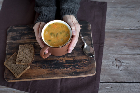 Woman hands holding mug of vegetable soup on wooden background - healthy winter vegetarian food, cozy warming soup.の写真素材