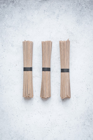 Soba noodles - traditional asian food ingredient. Bundle of buckwheat soba noodles on white concrete...
