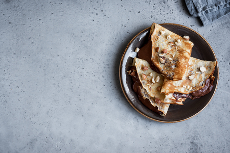 Crepes with chocolate spread and hazelnuts. Homemade thin crepes for breakfast or dessert on rustic background, copy space.の写真素材