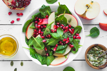 Homemade spinach, apple salad with pomegranate seeds on white wooden background. Heathy clean vegan raw food, fresh salad and ingredients.の写真素材
