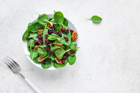 Spinach salad with  pecan nuts and dry cranberries on white background, copy space. Heathy clean vegan raw food, fresh salad.の写真素材