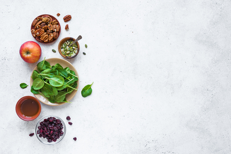 Healthy Salad Ingredients for cooking healthy vegan salad - baby spinach leaves, apple, pecan nuts, dry cranberries. Clean eating or diet food ingredients on white background, copy space.の写真素材