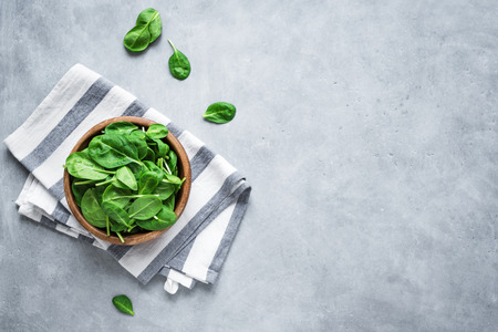 Baby spinach leaves in bowl on grey concrete background, top view, copy space. Clean eating, detox,...