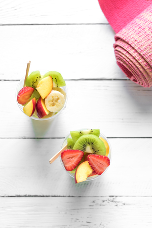 Feminine Sport and Healthy Lifestyle Concept. Pink yoga mat and Fruit and Berries Salad in plastic cup to go, copy space, top view.の写真素材
