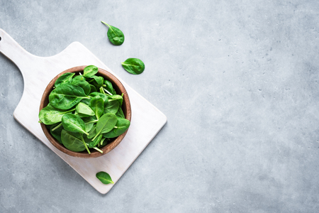 Baby spinach leaves in bowl on grey concrete background, top view, copy space. Clean eating, detox, diet food ingredient - green organic spinach.の写真素材