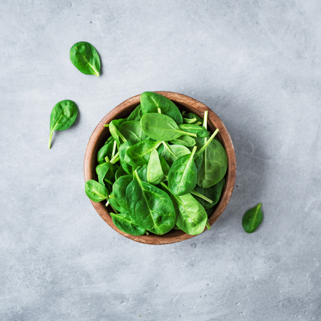 Baby spinach leaves in bowl on grey concrete background, top view, copy space. Clean eating, detox, diet food ingredient - green organic spinach.の写真素材