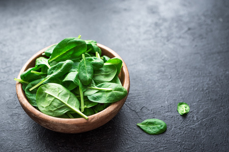 Baby spinach leaves in bowl on black background, top view, copy space. Clean eating, detox, diet food ingredient - green organic spinach.の写真素材