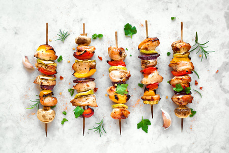 Grilled vegetable and chicken skewers with  bell peppers, zucchini, onion and mushrooms on white marble background, top view. Meat and vegetables kebabs on skewers.の写真素材