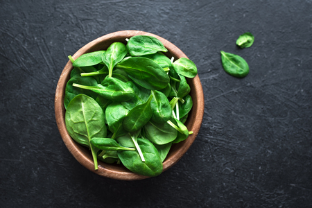 Baby spinach leaves in bowl on black background, top view, copy space. Clean eating, detox, diet food ingredient - green organic spinach.の写真素材