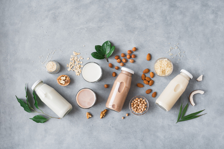 Various vegan plant based milk and ingredients on grey, top view, copy space. Dairy free milk substitute drink, healthy eating.の写真素材