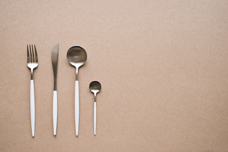 Set of stylish white and chrome cutlery on beige background, top view, copy space. Table set, menu...