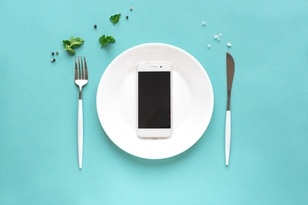 Smartphone on white plate with fork and knife. Food delivery concept on blue background, top view, copy space.の写真素材