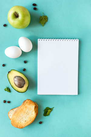 Avocado, egg and toast for breakfast on blue background with note book, top view, copy space. Healthy breakfast ingredients - egg, bread, avocado, apple and coffee beans.の写真素材