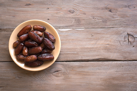 Dates on plate on wooden background, top view, copy space. Organic dates fruits.