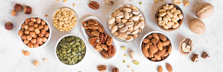 Various Nuts in  bowls on white background, top view, banner. Nuts assortment - pecans, hazelnuts, walnuts, pistachios, almonds, pine nuts, peanuts, pumpkin seeds.の写真素材
