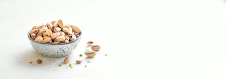 Pistachio nuts. Green salted pistachios in ceramic bowl on white background, copy space, banner.の写真素材