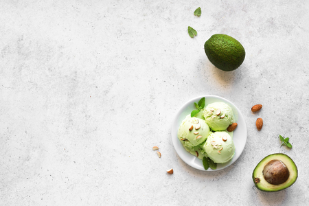Avocado Ice Cream on white stone background, top view, copy space. Green vegan avocado or pistachio gelato ice cream with almonds and mint leaves.の写真素材