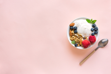 Greek yogurt with homemade granola and berries for healthy breakfast on pink pastel background, top view, copy space.の写真素材