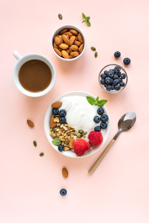 Greek yogurt with homemade granola and berries for healthy breakfast with coffee on pink pastel background, top view, copy space.の写真素材
