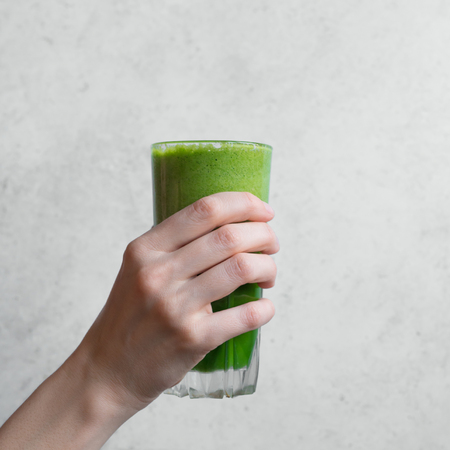 Green smoothie in hand. Female hand holding glass of green spinach detox smoothie, copy space.