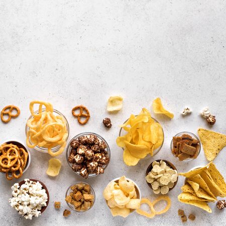 Assortment of Unhealthy Snacks: chips, popcorn, nachos, pretzels, onion rings in bowls, top view, copy space. Unhealthy eating concept.の写真素材