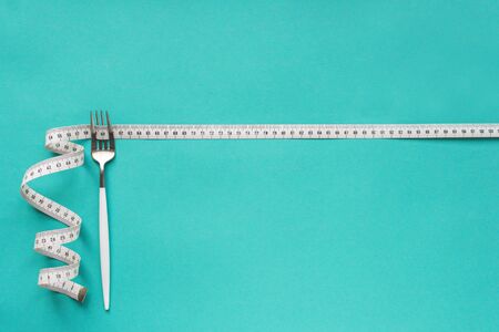 Fork and Measuring Tape on blue background, copy space. Diet, healthy lifestyle, weight loss concept...