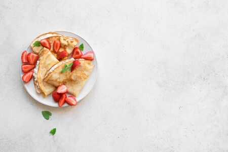 Crepes with ricotta cheese and fresh strawberries on white background, top view, copy space. Delicious crepes, thin pancakes.の写真素材