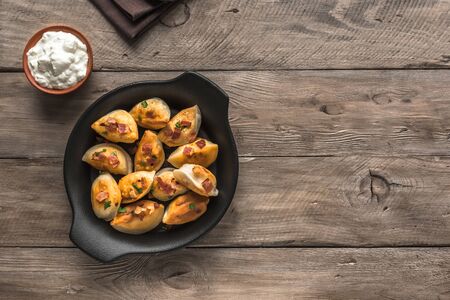 Fried dumplings stuffed with potato and meat (pierogi) sprinkled with bacon and  parsley and sour...