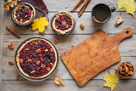 Autumn Pies on wooden background, top view, copy space. Homemade seasonal pastry - berries and pecan pies or tarts for Thanksgiving and autumn holidays.の写真素材