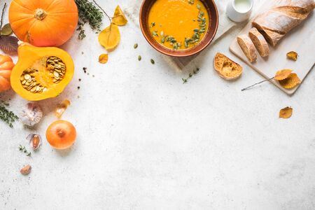 Pumpkin soup and organic pumpkins on white background, copy space. Seasonal autumn food - Spicy pumpkin soup with thyme and pumpkin seeds.の写真素材
