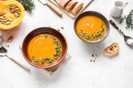 Pumpkin soup and organic pumpkins on white background, copy space. Seasonal autumn food - Spicy pumpkin soup with thyme and pumpkin seeds.の写真素材