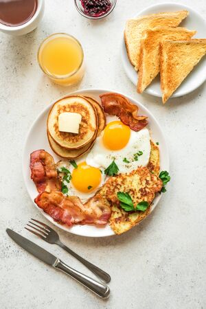 Full American Breakfast on white, top view, copy space. Sunny side fried eggs, roasted bacon, hash brown, pancakes, orange juice and coffee for breakfast.の写真素材