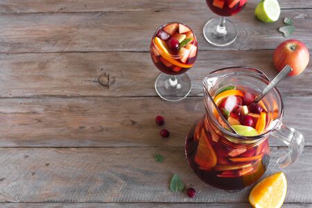 Red wine sangria or punch with fruits and ice in pitcher and glasses. Homemade refreshing fruit sangria on wooden background, copy space.の写真素材