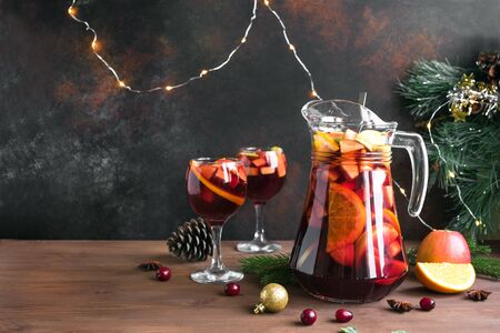 Christmas sangria or punch in glasses and pitcher. Homemade red wine fruit sangria and christmas festive decor on wooden background, copy space.の写真素材
