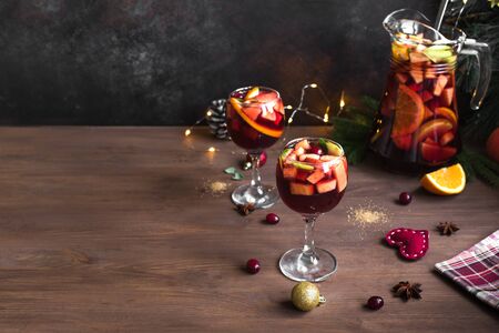 Christmas sangria or punch in glasses and pitcher. Homemade red wine fruit sangria and christmas festive decor on wooden background, copy space.の写真素材