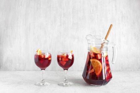 Red wine sangria or punch with fruits and ice in glasses and pitcher. Homemade refreshing fruit sangria on white background, copy space.の写真素材