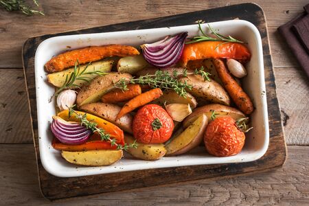 Oven roasted vegetables with spices and herbs in baking dish on wooden, top view. Vegetarian organic autumn meal - baked vegetables.の写真素材