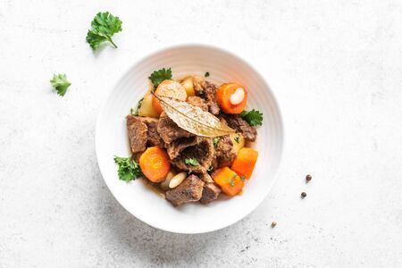 Beef meat stewed with potatoes, carrots and spices on white background, top view, copy space. Homemade winter comfort food - slow cooked meat stew.の写真素材